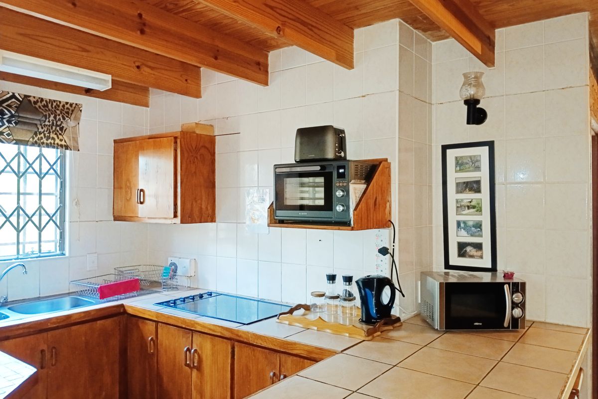 A functional kitchen featuring wooden cabinetry, tiled countertops, and exposed timber ceiling beams, offering a classic rustic aesthetic with ample workspace.