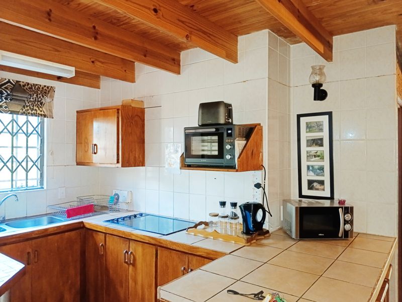 A functional kitchen featuring wooden cabinetry, tiled countertops, and exposed timber ceiling beams, offering a classic rustic aesthetic with ample workspace.