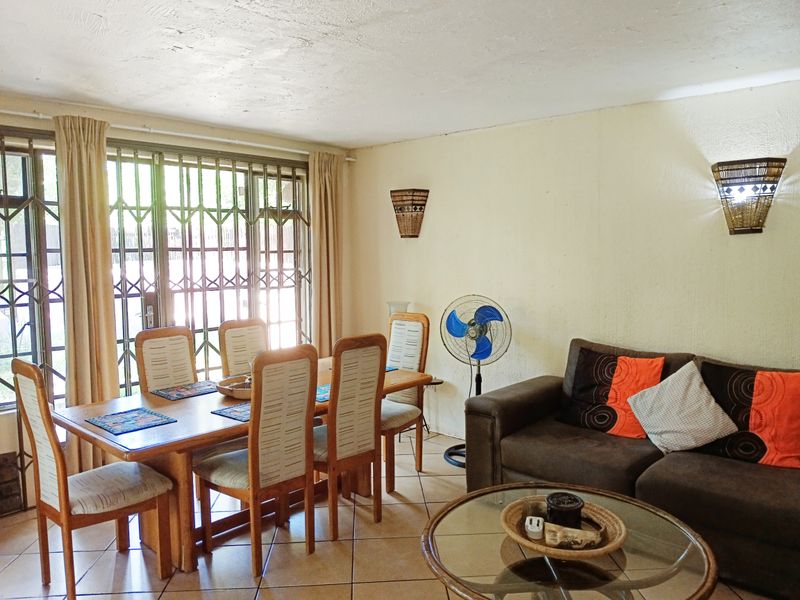 Open plan living and dining area featuring tiled flooring, wall-mounted lighting, and a sliding door with security gate access to the exterior.