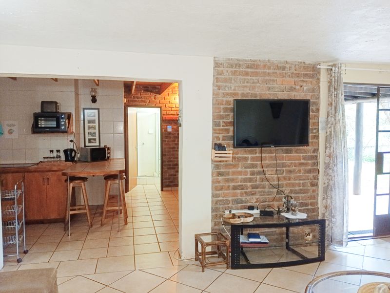 Open plan living area featuring an exposed brick feature wall, tiled flooring, and an adjoining kitchen space with built-in cabinetry.
