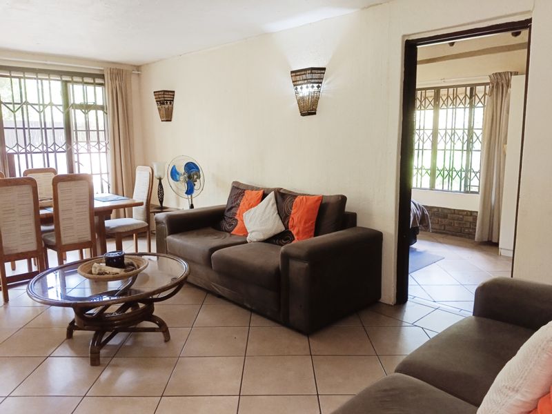 Open-plan living and dining area featuring tiled flooring, wall-mounted lighting, and access to an adjacent bedroom through a doorway.
