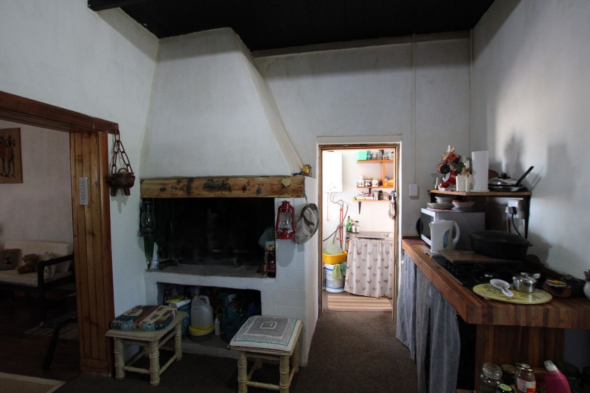 Rustic kitchen area featuring a large built-in masonry fireplace, wooden countertops, and an adjacent scullery or utility space.