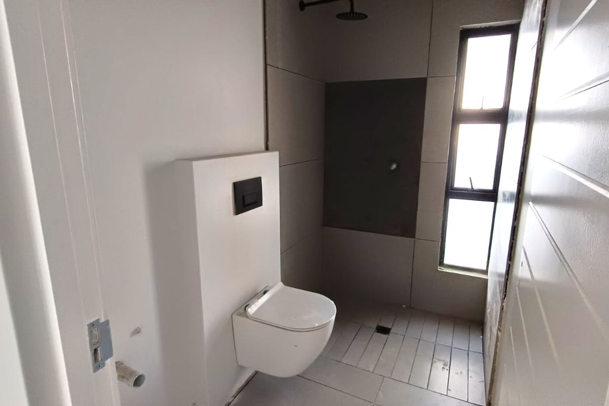 A modern, minimalist bathroom featuring a wall-hung toilet with a concealed cistern and a walk-in shower with dark tiled accents.