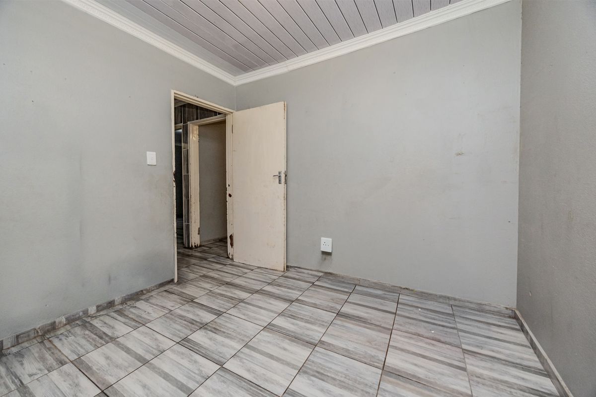 An empty bedroom featuring tiled flooring, a panelled ceiling with coving, and neutral wall finishes, providing a blank canvas for renovation.