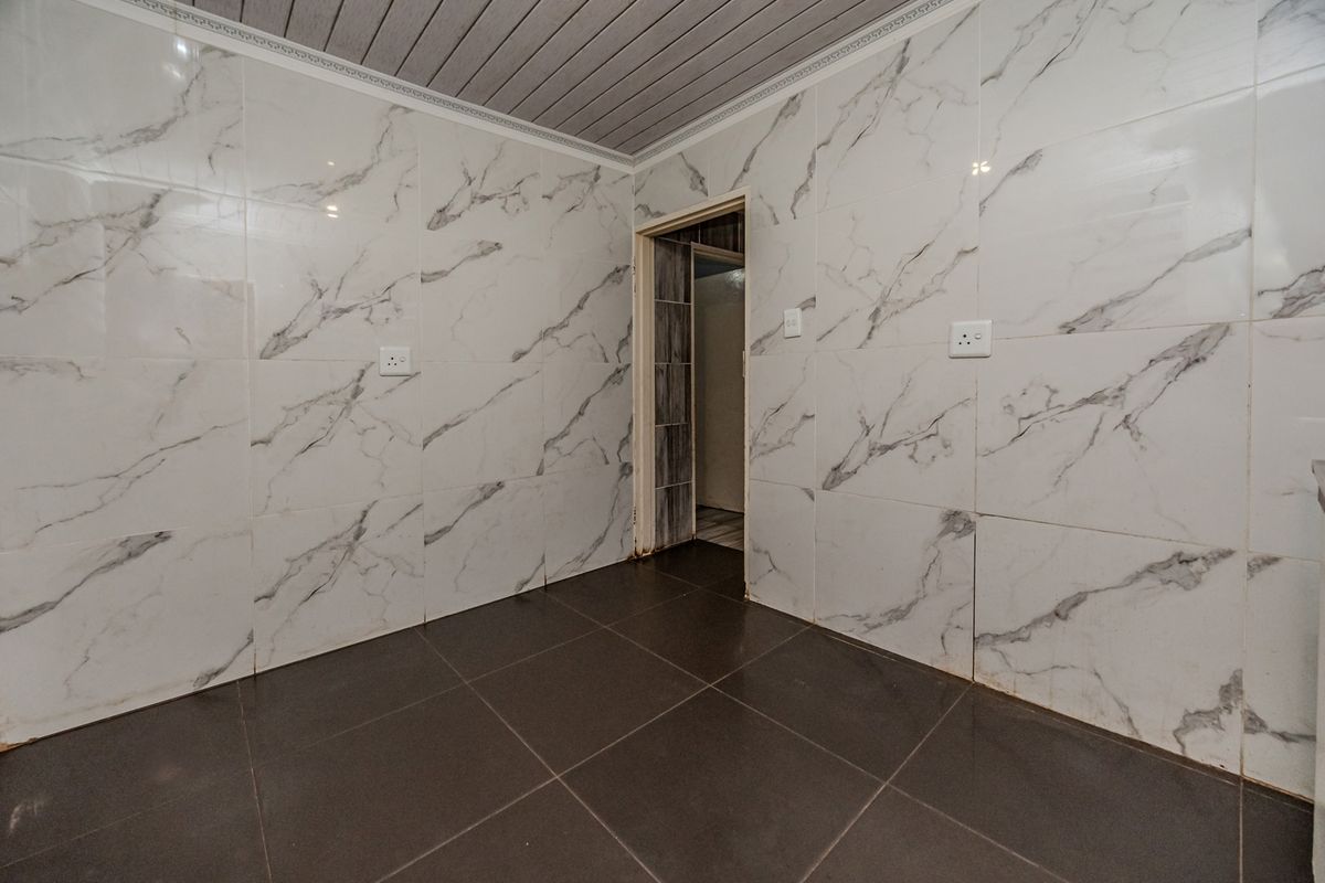 An empty kitchen space featuring marble-effect wall tiling, dark floor tiles, and a PVC panelled ceiling, ready for custom cabinetry and appliance installation.
