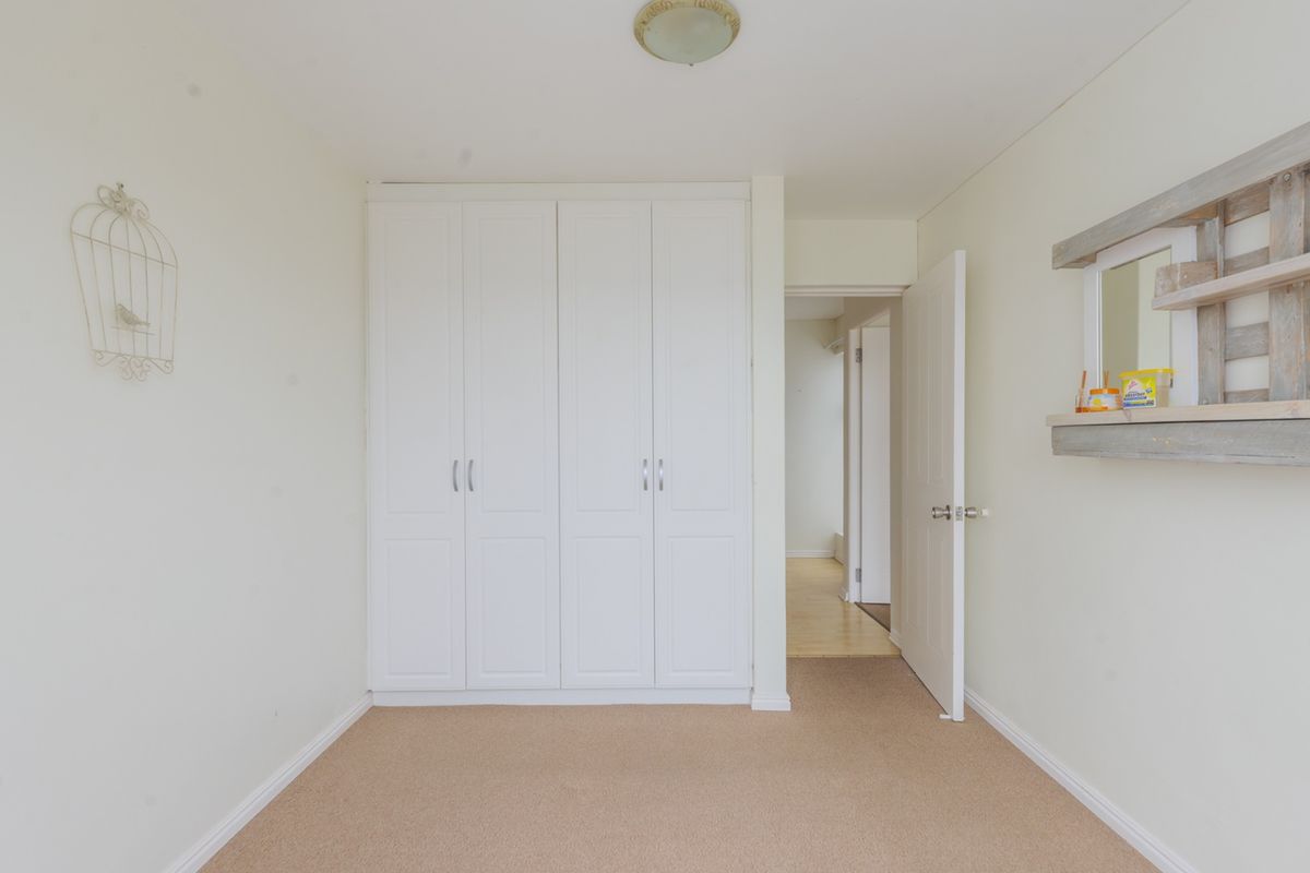 A clean, empty bedroom featuring neutral carpet flooring and a white built-in wardrobe with classic panel detailing.