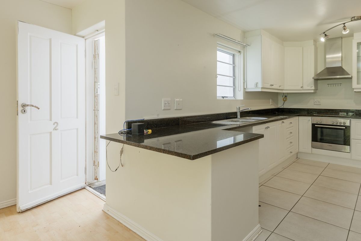 A clean, functional kitchen featuring white cabinetry, dark granite countertops, built-in oven, stainless steel extractor fan, and tiled flooring with direct exterior access.