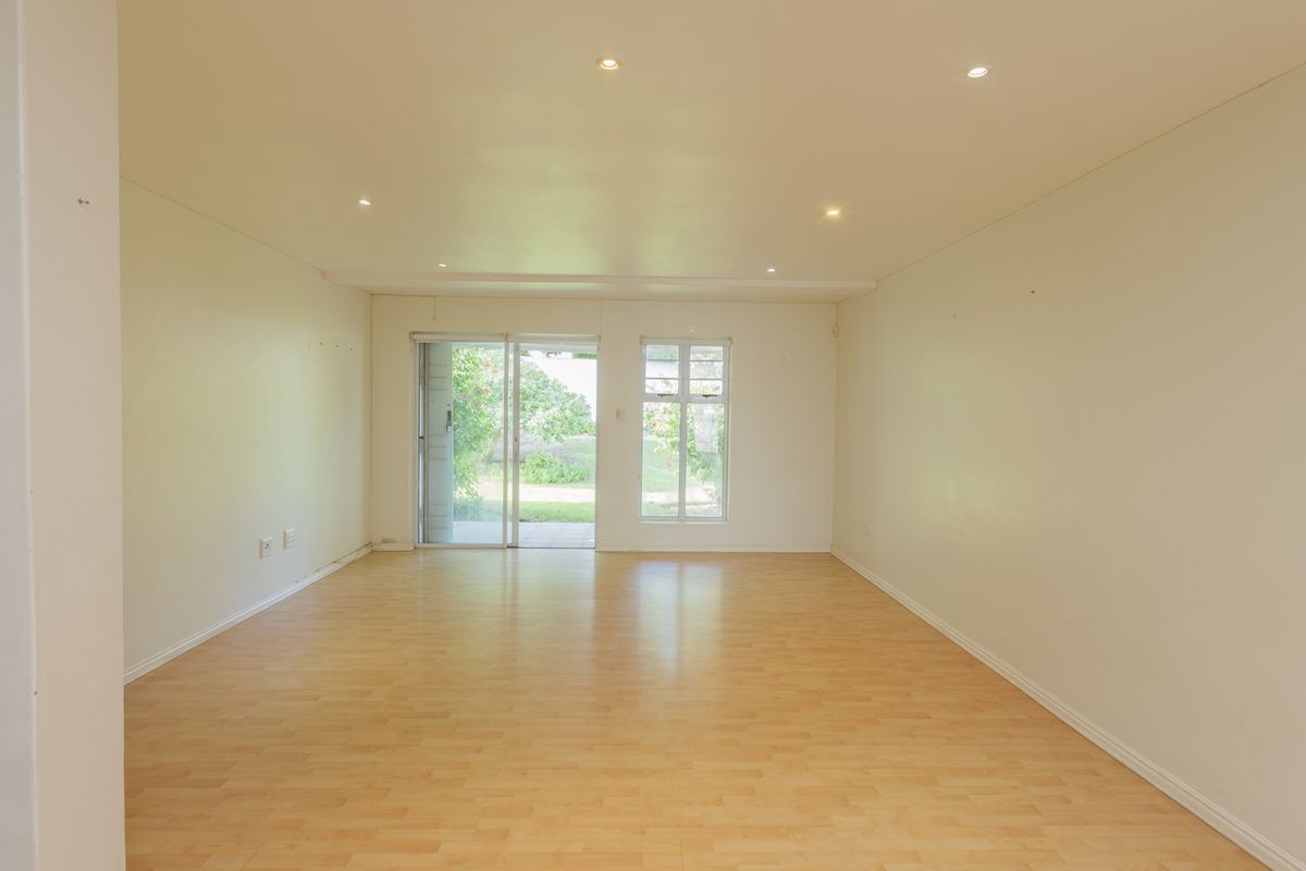 A spacious, empty living room featuring light laminate flooring, recessed downlights, and a sliding glass door providing access to the exterior.