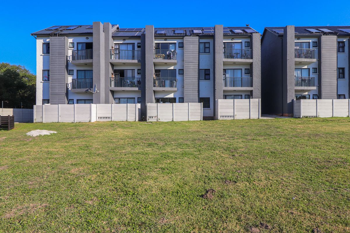 Rear view of a multi-story apartment complex featuring private balconies, concrete boundary walls, and solar panels installed on the roof.