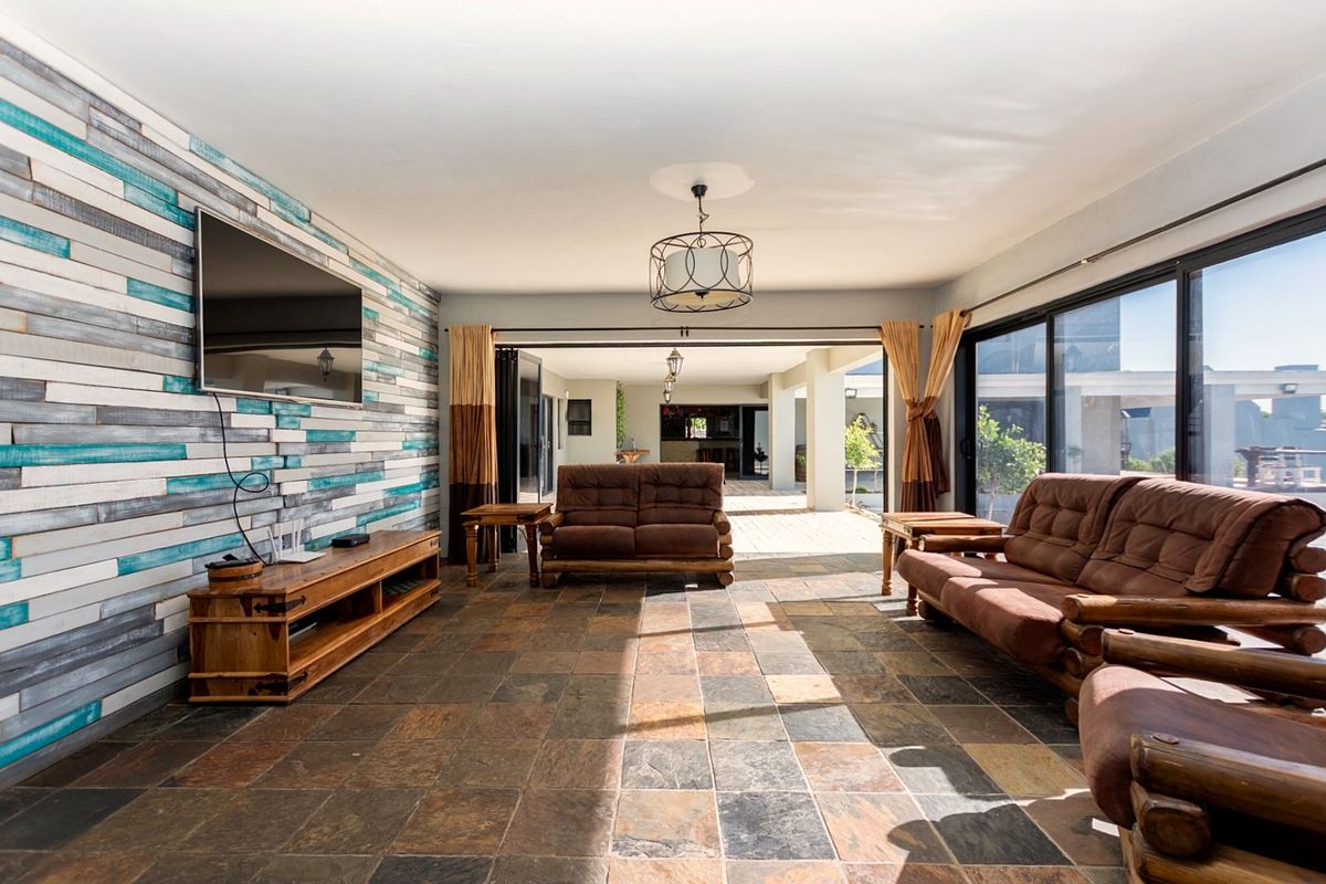 Spacious living area featuring natural stone tile flooring, a decorative wood-paneled feature wall, and large sliding glass doors opening to a covered patio.