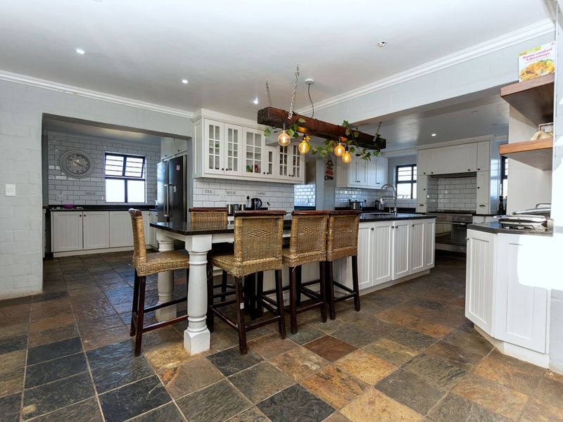 Spacious open-plan kitchen featuring white cabinetry, subway tile backsplash, dark countertops, a central island with seating, and rustic overhead lighting.