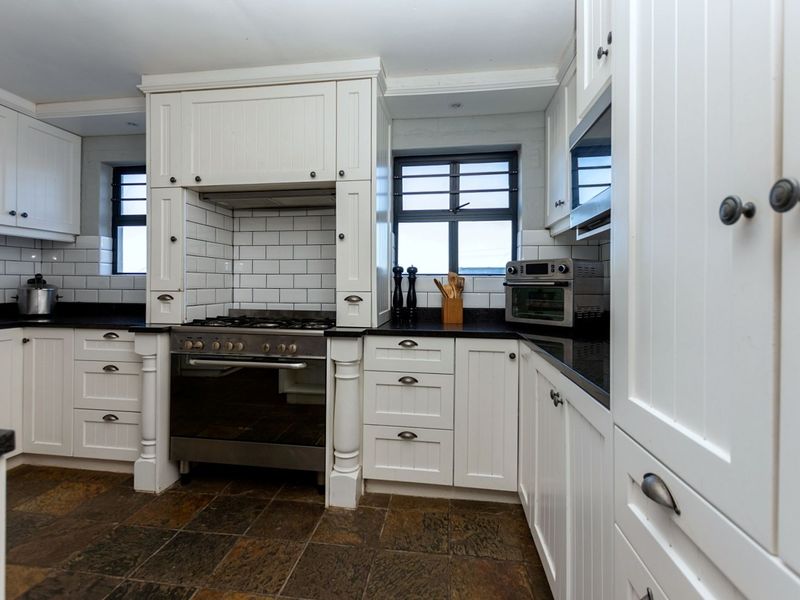 A well-appointed kitchen featuring white cabinetry, dark stone countertops, a built-in gas stove with extractor hood, and classic subway tile backsplash.