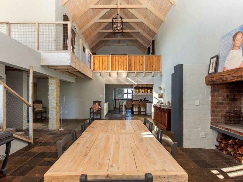 Spacious open-plan living and dining area featuring a vaulted timber-truss ceiling, mezzanine level, and a large rustic brick fireplace.