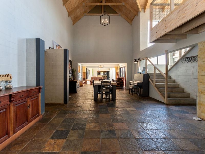 Spacious open-plan living area featuring high vaulted timber ceilings, exposed brick walls, slate tile flooring, and a mezzanine level with a wooden staircase.