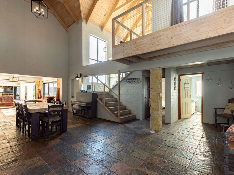 Spacious open-plan living area featuring high vaulted timber ceilings, a mezzanine level with wire balustrading, stone-tiled flooring, and a central stone-clad pillar.