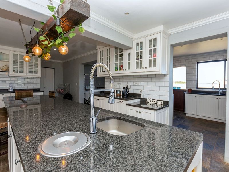 A spacious kitchen featuring a large granite-topped island with a prep sink, white cabinetry, subway tile backsplash, and a secondary scullery area.