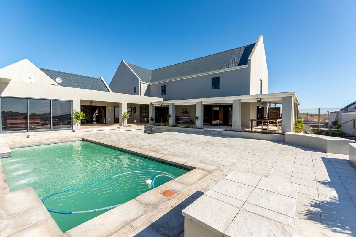 Spacious rear exterior featuring a large swimming pool, expansive paved patio area, and covered veranda attached to the modern multi-gabled residence.