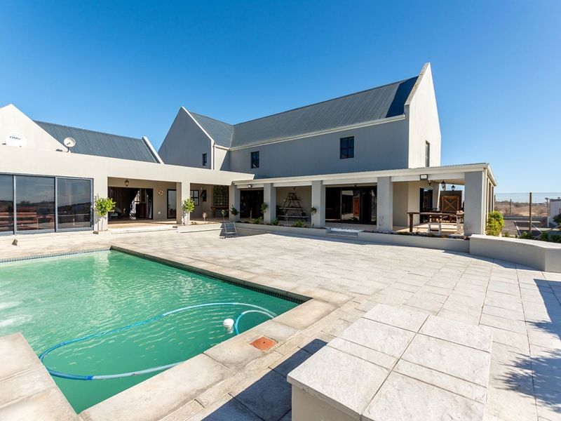 Spacious rear exterior featuring a large swimming pool, expansive paved patio area, and covered veranda attached to the modern multi-gabled residence.