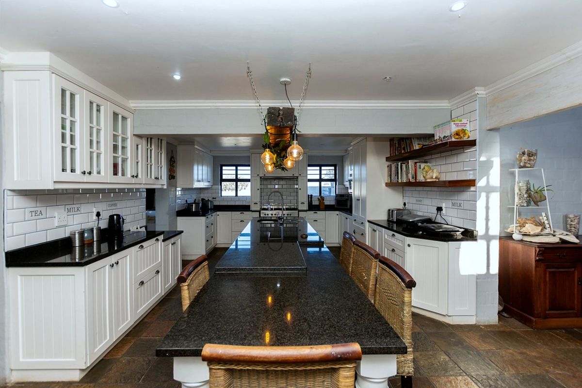Spacious kitchen featuring a large central island with granite countertops, white cabinetry, subway tile backsplash, and integrated shelving.