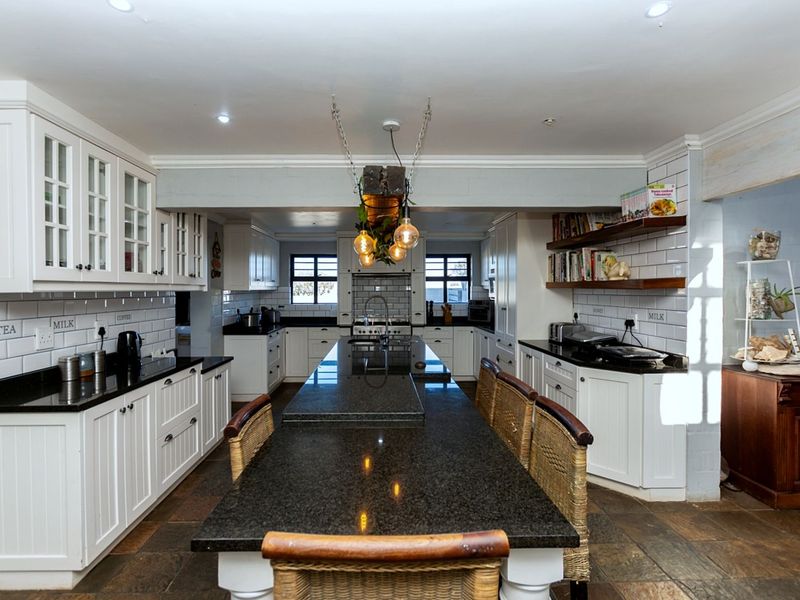 Spacious kitchen featuring a large central island with granite countertops, white cabinetry, subway tile backsplash, and integrated shelving.