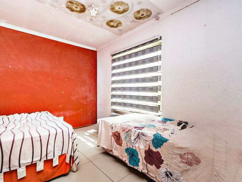 A bedroom featuring tiled flooring, zebra blinds, and a decorative ceiling, currently requiring cosmetic updates and wall repairs.