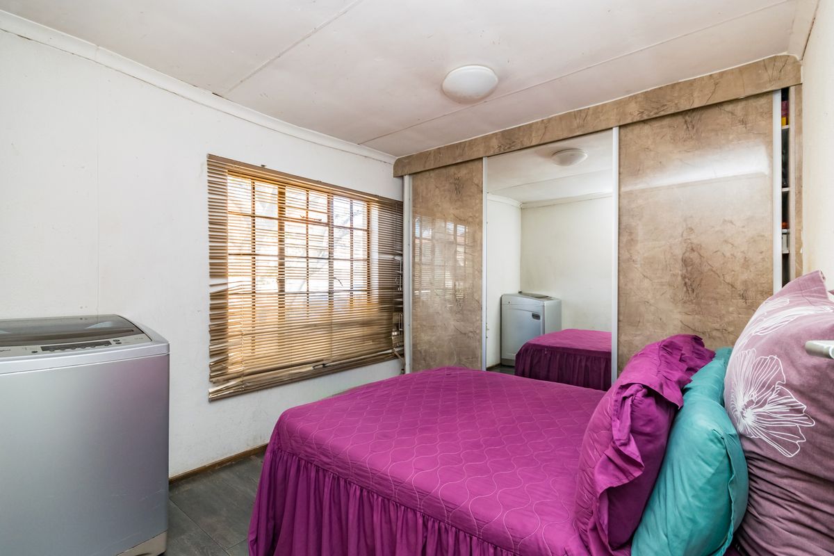 A bedroom featuring built-in wardrobes with mirrored sliding doors and window blinds. The space requires cosmetic updates to improve its overall condition.