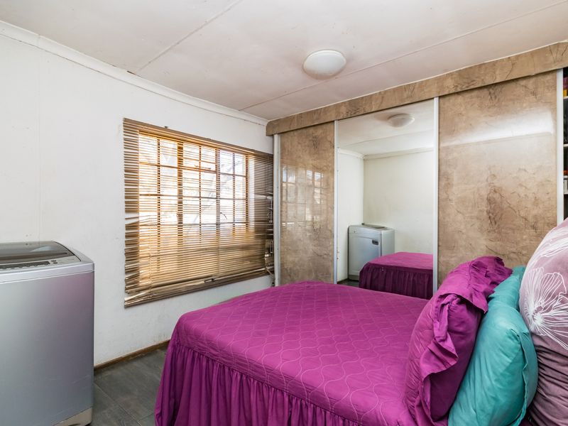 A bedroom featuring built-in wardrobes with mirrored sliding doors and window blinds. The space requires cosmetic updates to improve its overall condition.