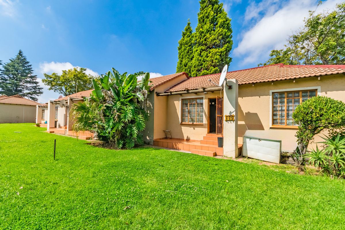 Rear view of a townhouse featuring a small tiled patio, lawn area, and traditional terracotta roof tiles.