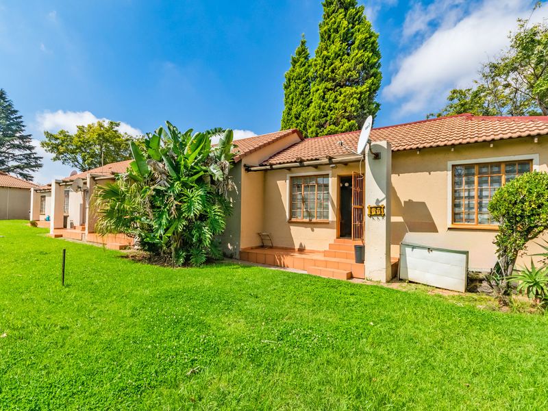 Rear view of a townhouse featuring a small tiled patio, lawn area, and traditional terracotta roof tiles.
