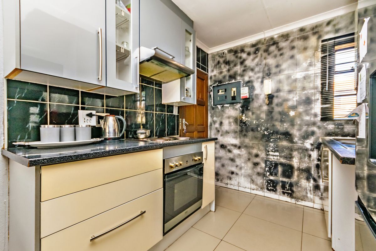 A compact kitchen featuring built-in cabinetry, an oven, and hob, currently requiring significant cosmetic refurbishment due to visible wall damage and wear.