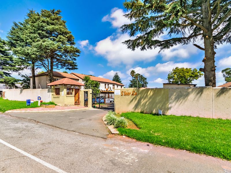 Street view of the complex entrance featuring a security gate, guard house, and perimeter wall with electric fencing.