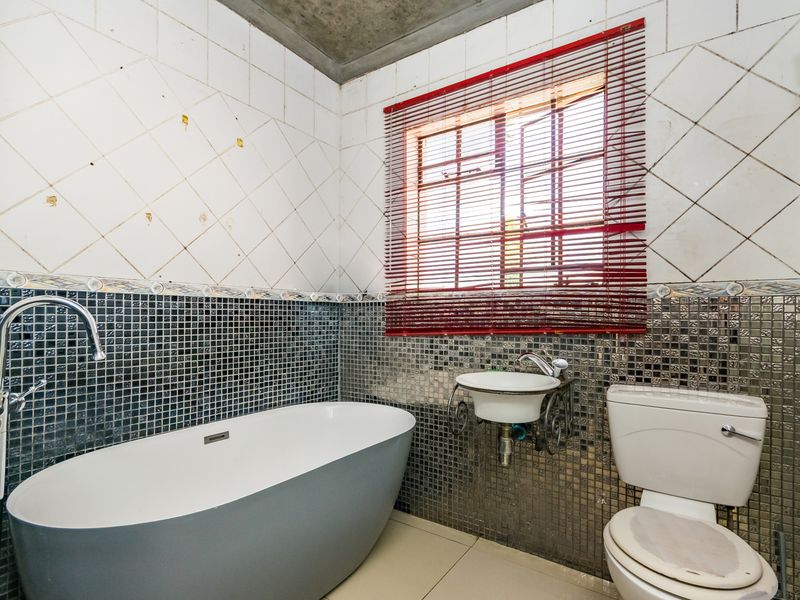 A bathroom featuring a freestanding bathtub, wall-mounted basin, and toilet, with mosaic tile accents and an exposed concrete ceiling.