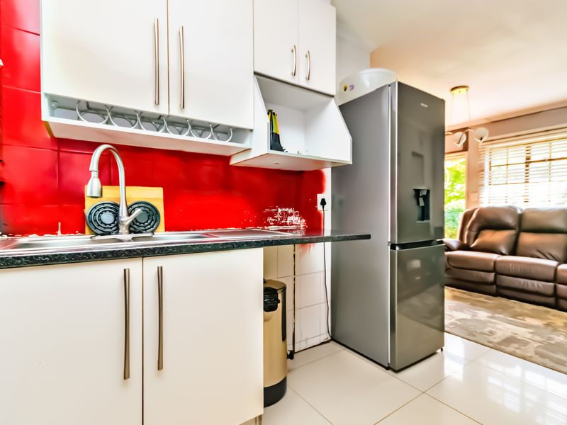Open plan kitchen area featuring white cabinetry, granite countertops, and a vibrant red tiled backsplash, flowing into the adjacent living space.