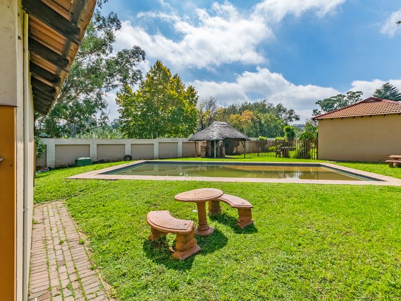 Outdoor pool area featuring a swimming pool, a thatched lapa, and a perimeter wall, set within a spacious garden.