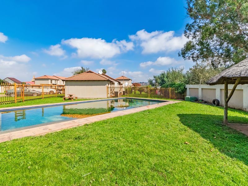 Outdoor pool area featuring a swimming pool with paved surround, a thatched lapa, and perimeter fencing in a residential townhouse setting.