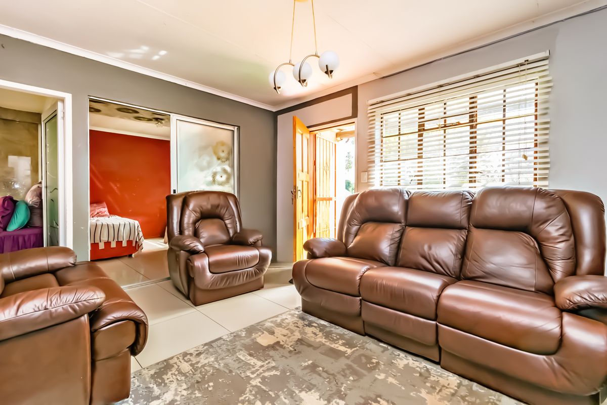 A living room area featuring tiled flooring, a sliding door leading to an adjacent room, and venetian blinds on the window.