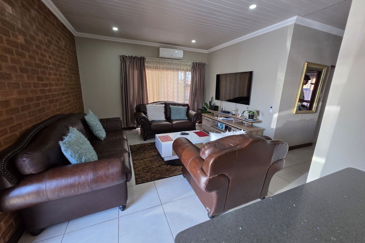 A comfortable living room featuring tiled flooring, a brick feature wall, recessed downlighting, and a wall-mounted air conditioning unit.