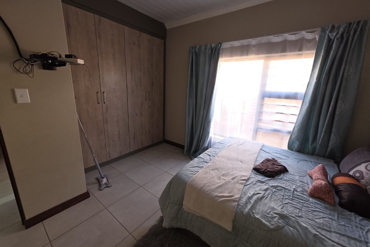 A bedroom featuring built-in wooden cabinetry, tiled flooring, and a window with curtains, providing a functional and well-maintained living space.