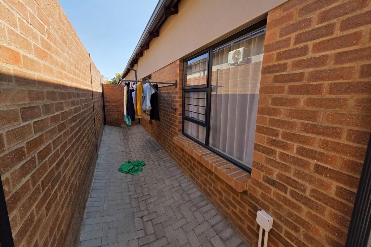 A side exterior walkway featuring brick paving, face brick walls, and a wall-mounted drying rack, providing functional outdoor utility space.