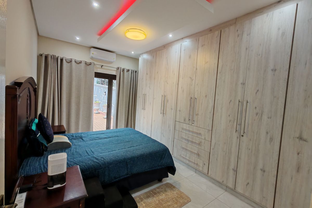 Spacious bedroom featuring extensive built-in light wood-grain cabinetry, recessed ceiling lighting with accent features, tiled flooring, and direct access to an outdoor patio area.