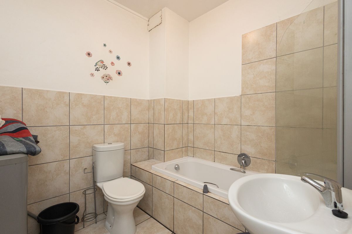 A functional bathroom featuring a built-in bathtub, pedestal basin, and toilet with neutral wall and floor tiling.