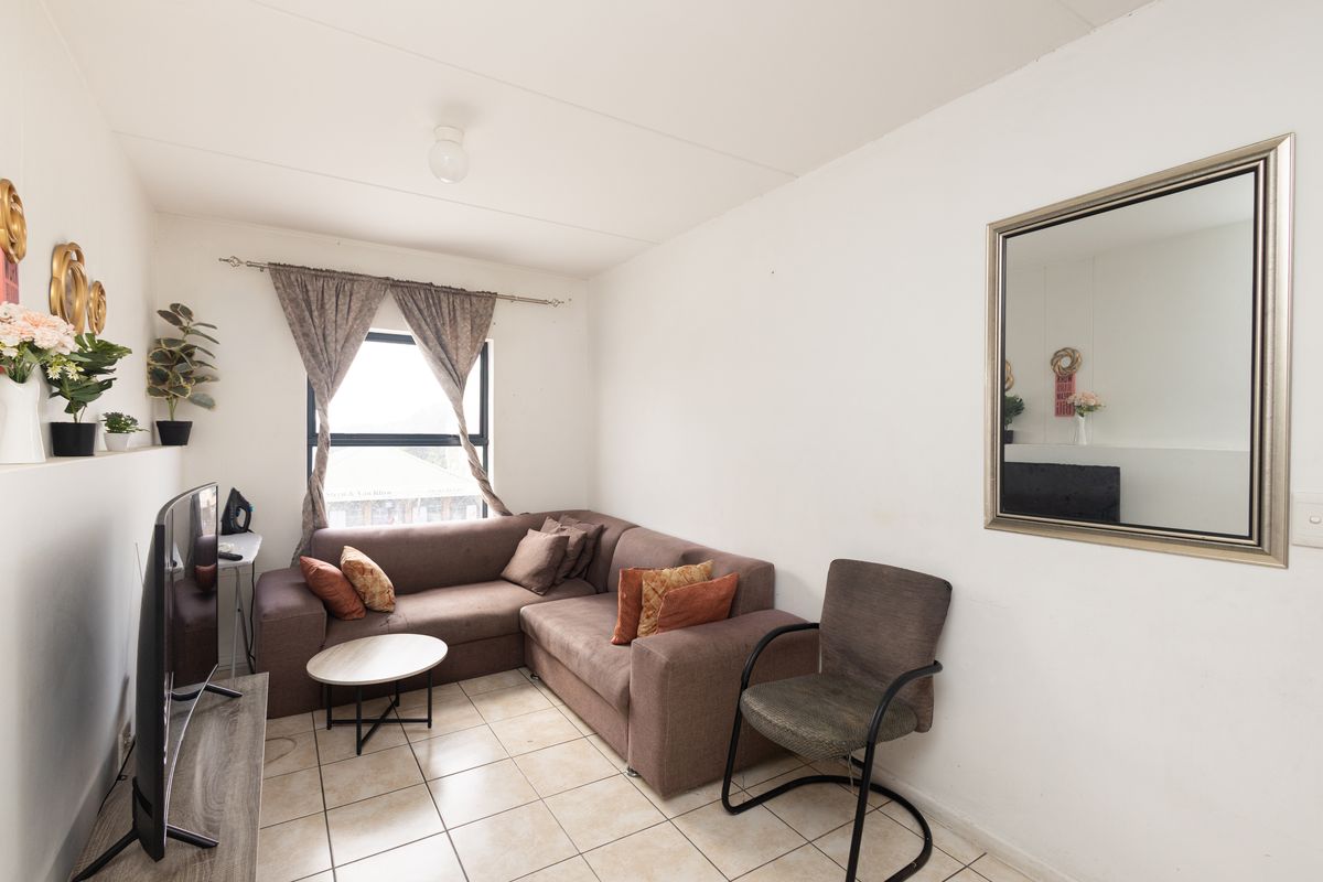 A compact living room featuring tiled flooring and a window with curtain rod, providing a functional space for relaxation.