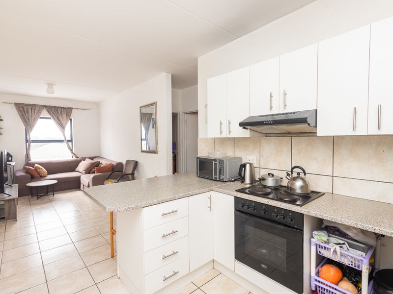 Open-plan kitchen and living area featuring white cabinetry, built-in oven, hob, extractor fan, and tiled flooring throughout.