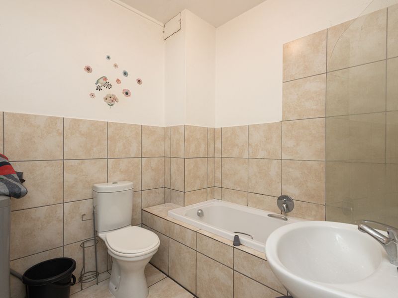 A functional bathroom featuring a built-in bathtub, pedestal basin, and toilet with neutral wall and floor tiling.