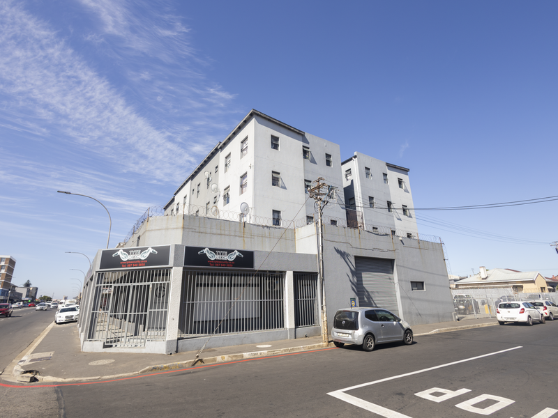 Exterior view of a multi-story apartment building featuring a ground-level commercial space with security gates and street-level access.