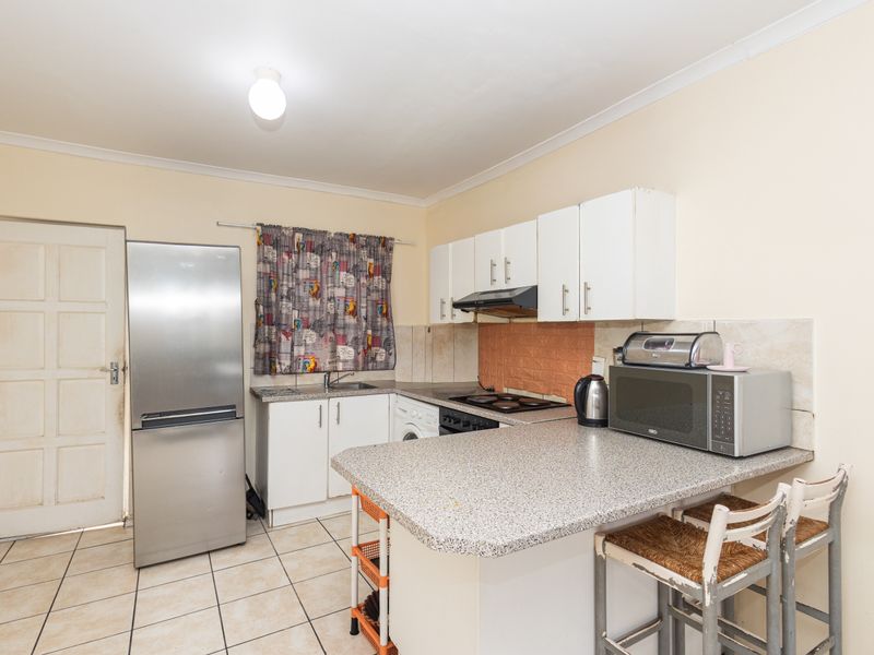 Functional kitchen featuring a breakfast bar, built-in cabinetry, integrated hob, and tiled flooring with direct access to an exterior door.