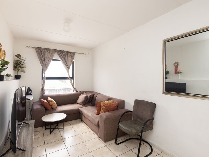 A compact living room featuring tiled flooring and a window with curtain rod, providing a functional space for relaxation.
