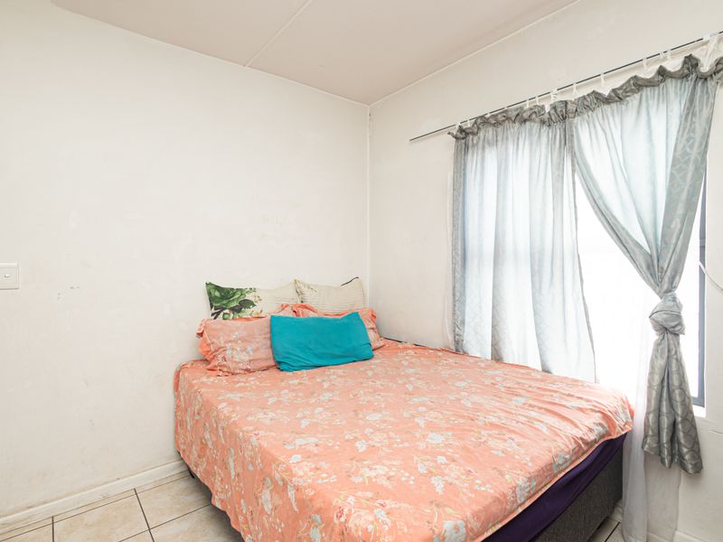 A compact bedroom featuring tiled flooring and a window with curtain track, requiring cosmetic updates to the wall finishes.