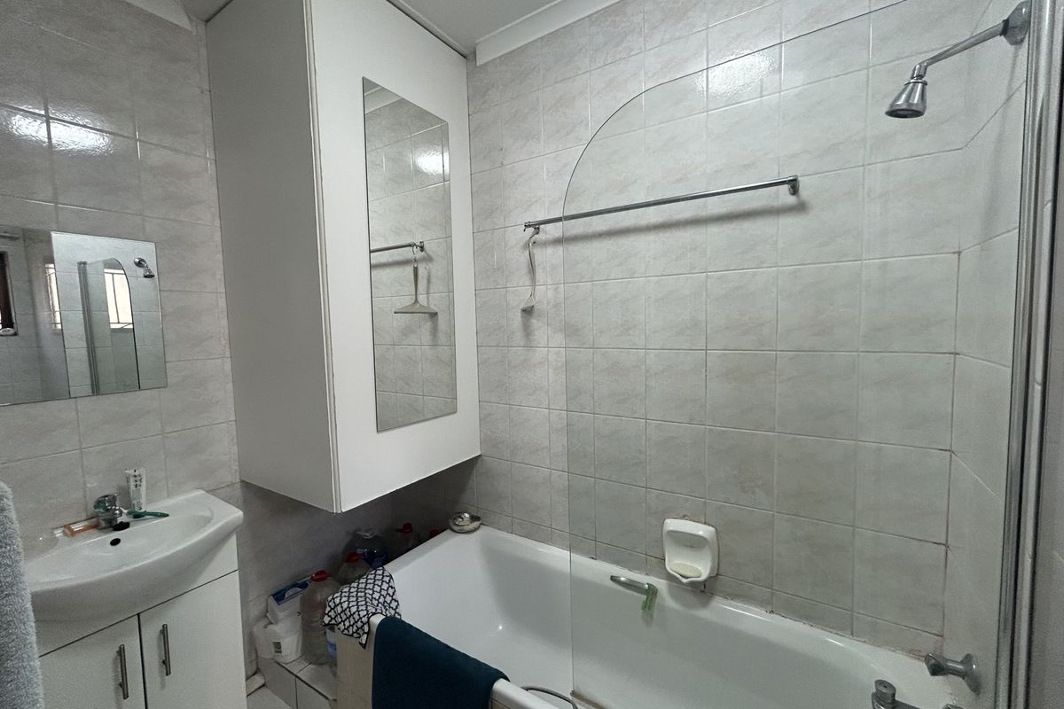 A functional bathroom featuring a bathtub with a shower head, glass screen, wall-mounted vanity with basin, and full-height wall tiling.