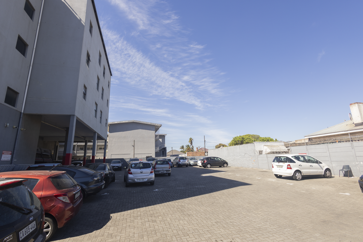 An outdoor paved parking area located at the rear of the apartment building, enclosed by a perimeter wall with security fencing.